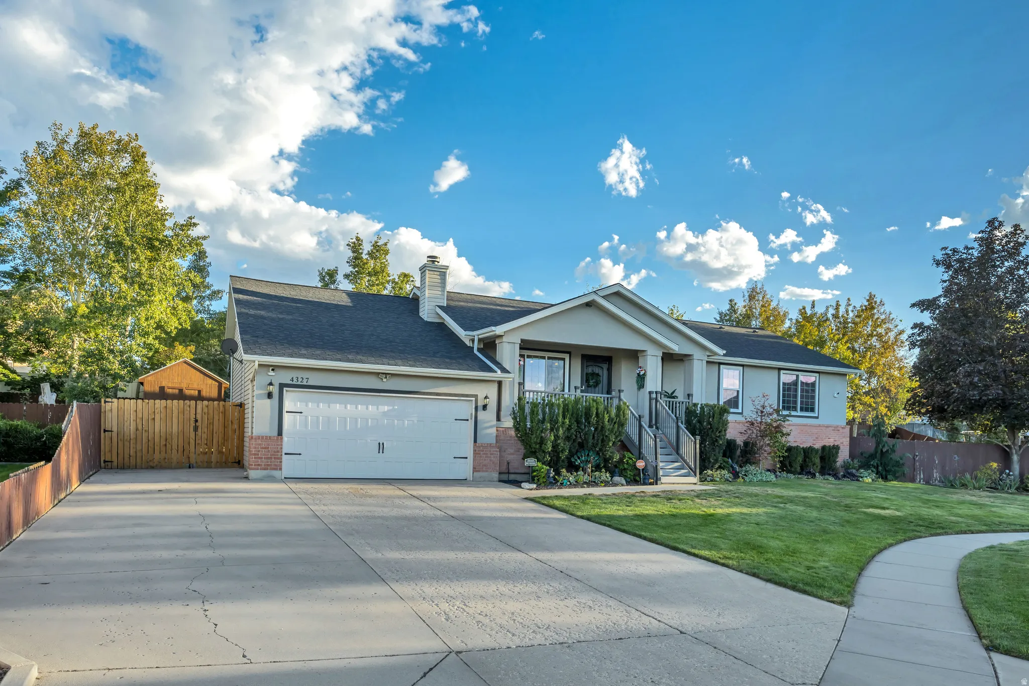 Light-colored exterior siding with brick accents, attached two-car garage, mature landscaping, concrete driveway, and a front walkway