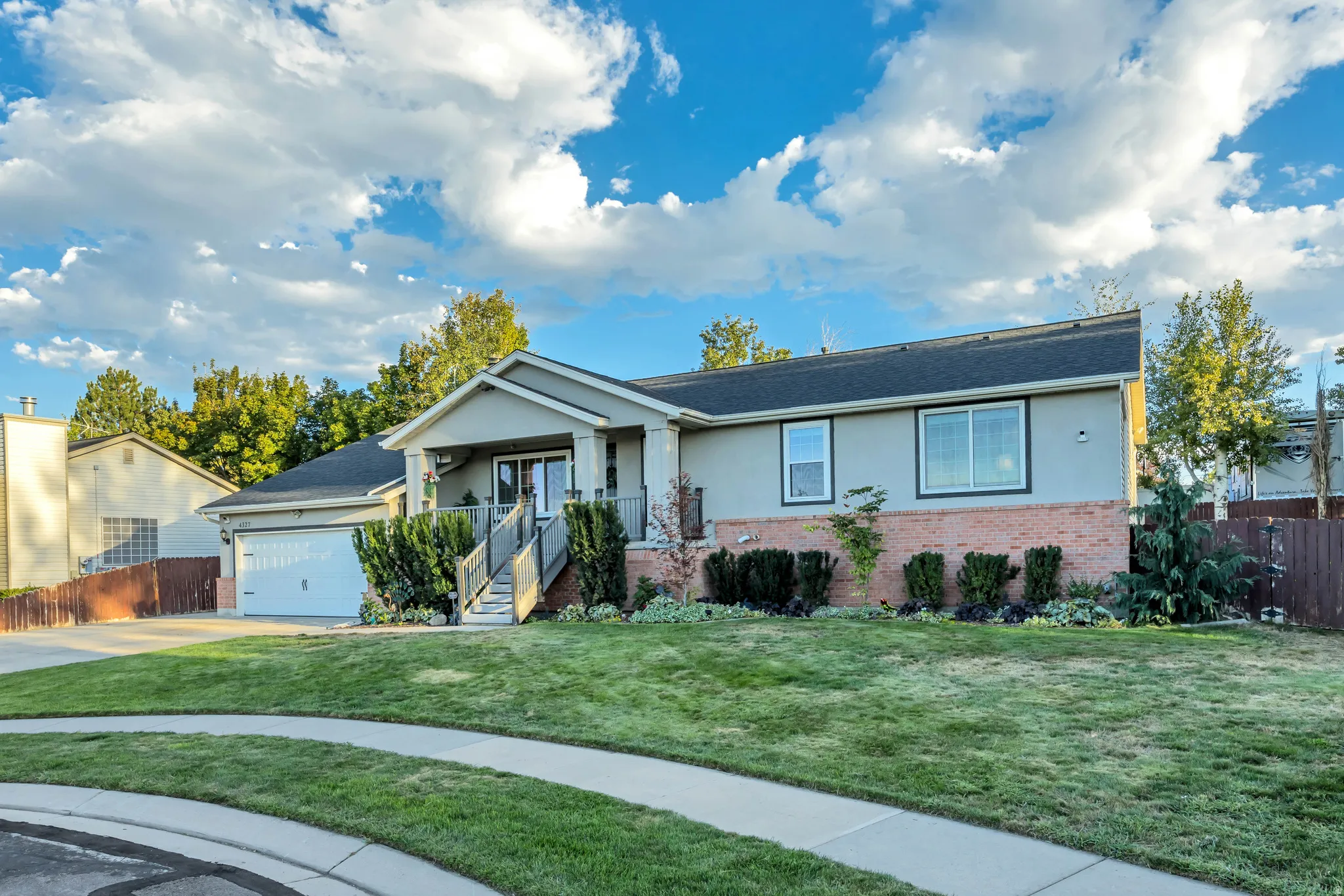 Exterior featuring a two-car garage, covered porch, brick detailing, and mature landscaping