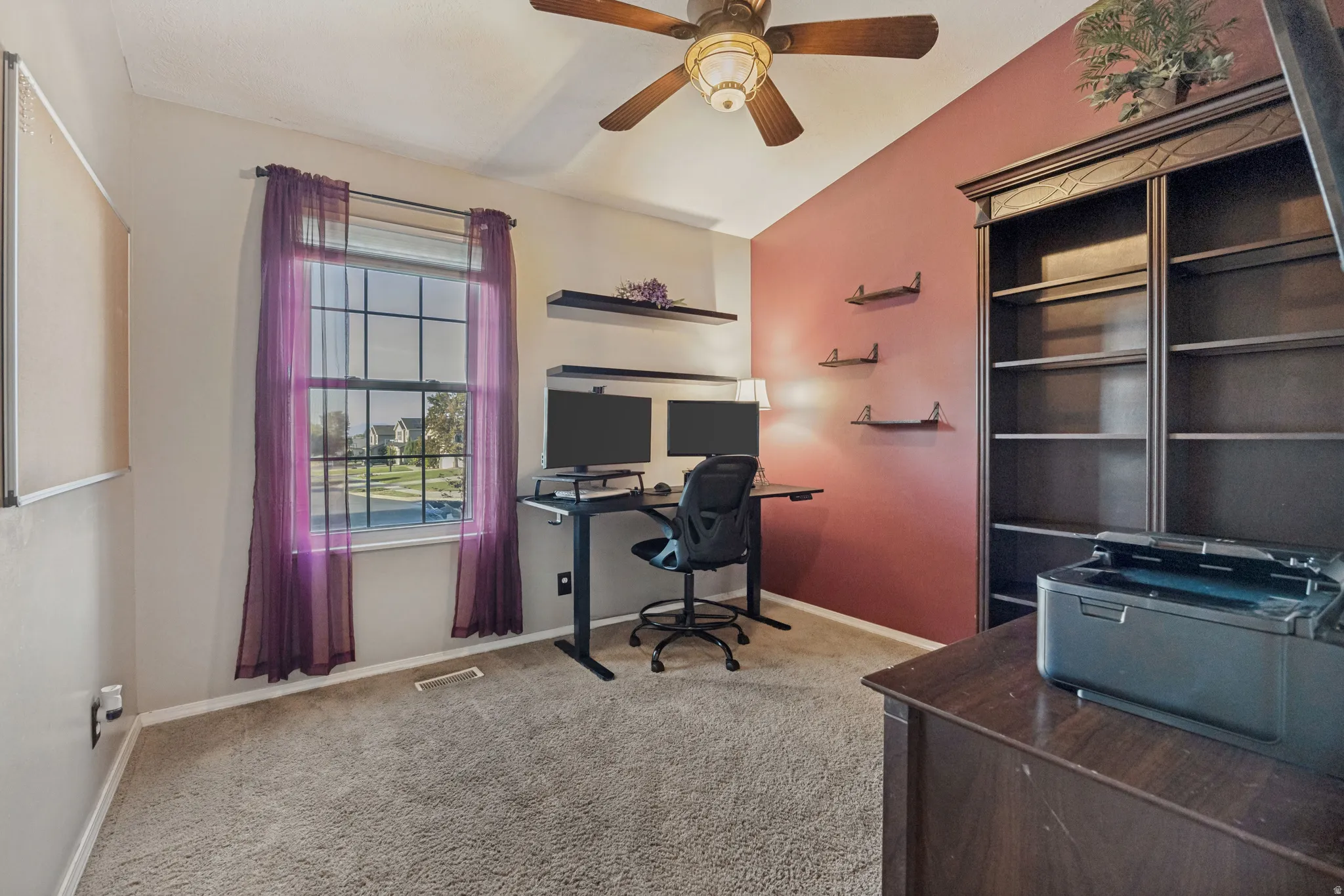 Carpeted room featuring a ceiling fan, a window with grid panes, and built-in shelving