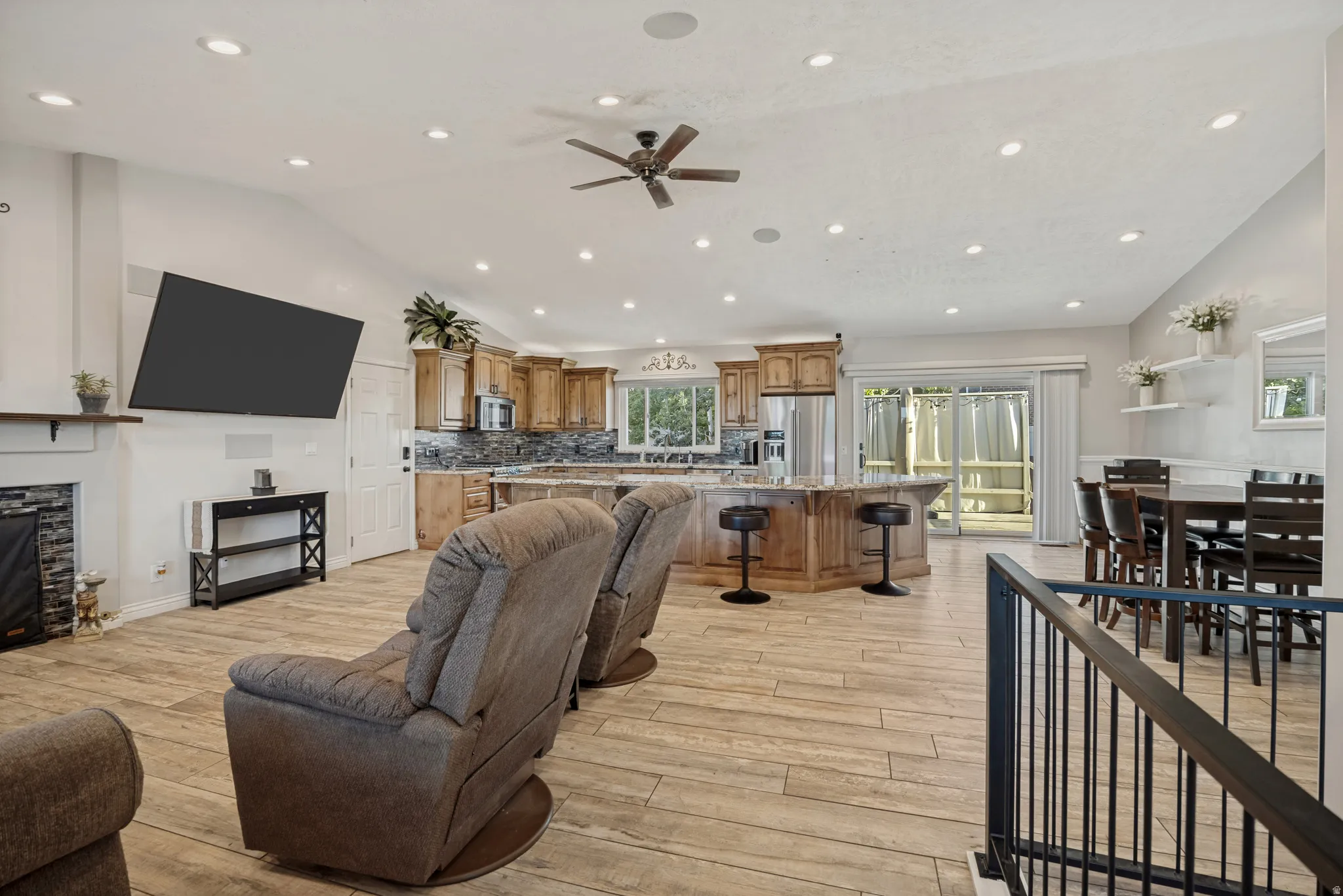 Open-concept living space featuring wood-finish flooring, recessed lighting, a stone-accented fireplace, and a kitchen island with seating