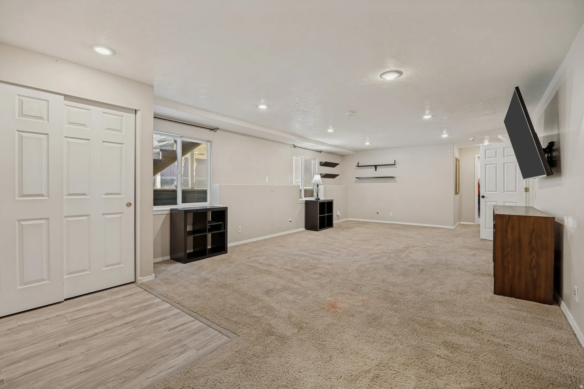 Recessed lighting illuminates this expansive space, featuring light-toned carpeting and wood-finish flooring