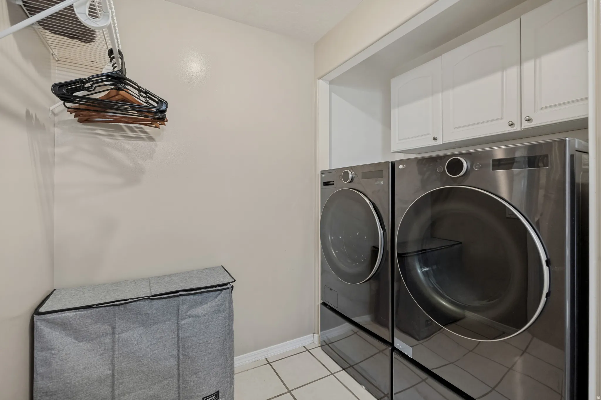 Dedicated laundry area featuring a front-loading washer and dryer, white cabinetry, and tiled flooring