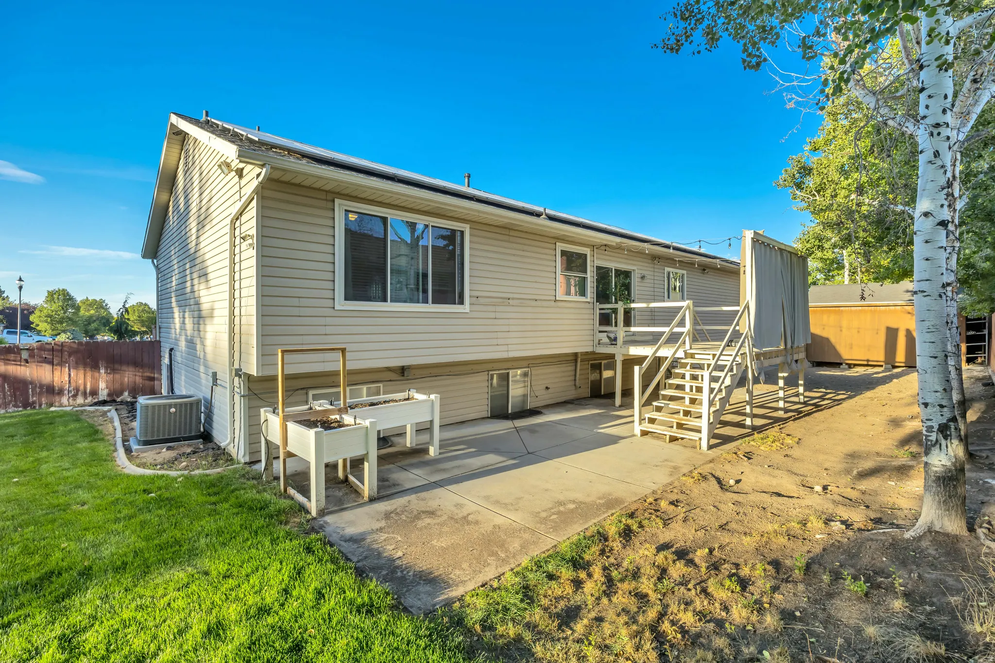 Rear exterior featuring light-colored siding, a concrete patio, and a wooden deck with stairs