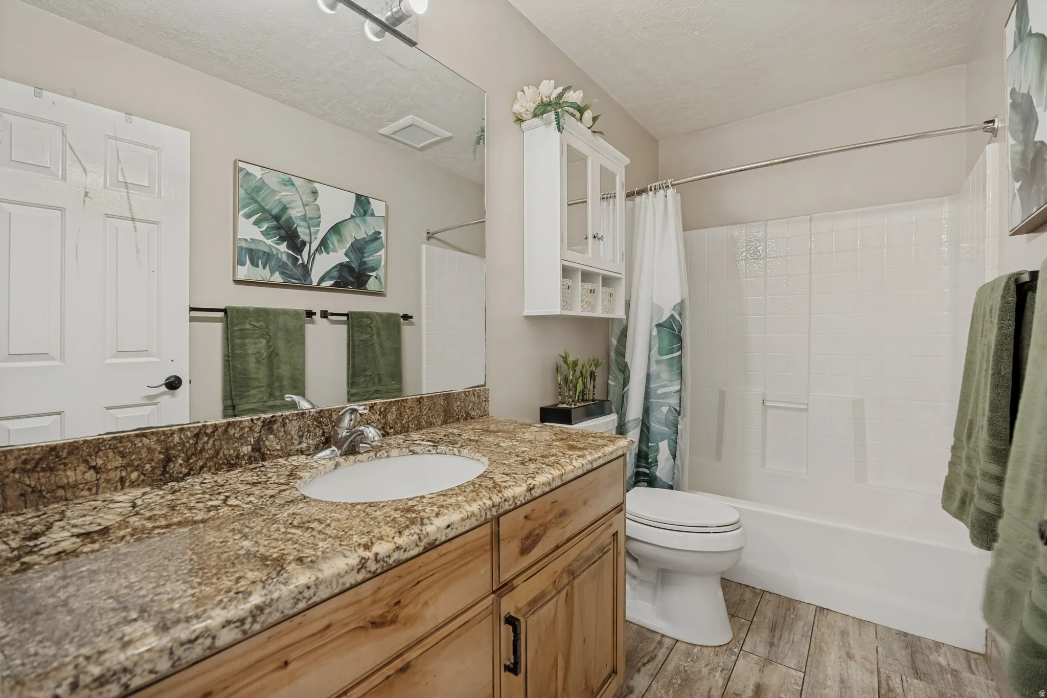 Granite-style countertop with an undermount sink, wood-finish vanity, wood-finish flooring, and a white tub with white tile-style surround