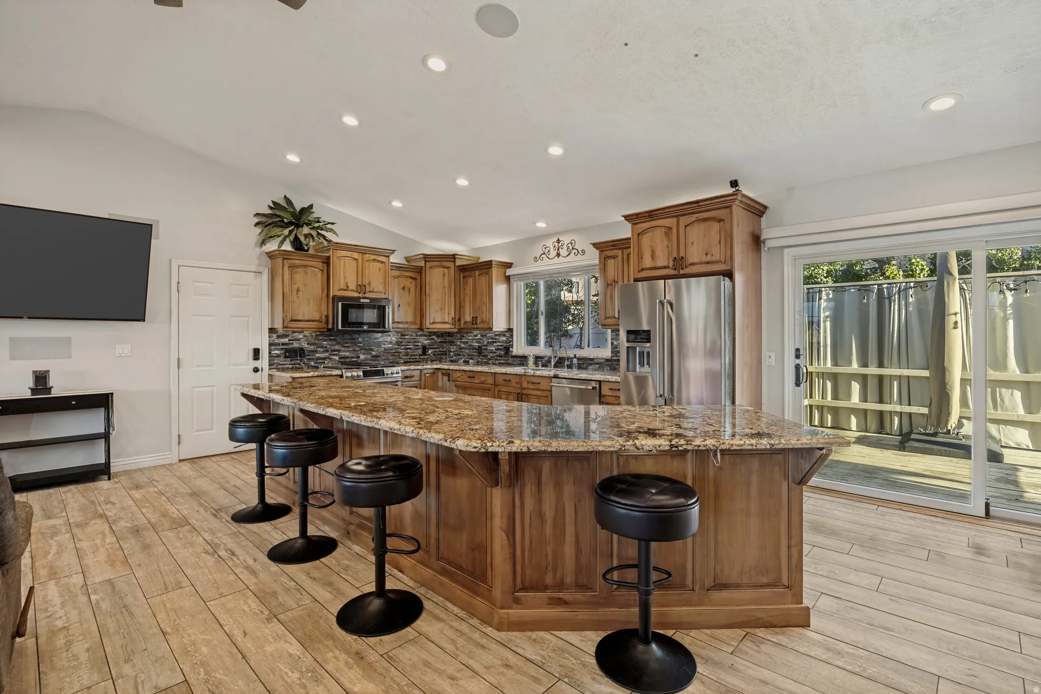 Kitchen featuring wood cabinetry, stainless steel appliances, a stone countertop island, and wood-finish flooring