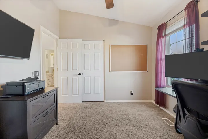 Vaulted ceiling with a ceiling fan, carpet flooring, and a window with a built-in desk