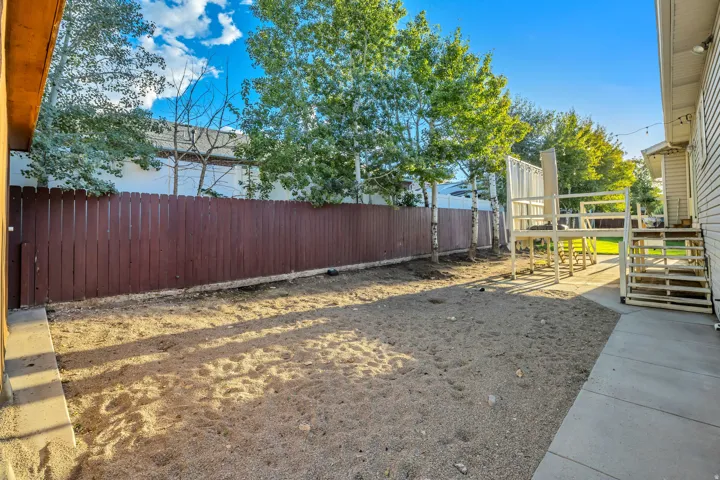 Spacious backyard with a wood privacy fence, concrete patio, multi-level deck structure, and mature trees