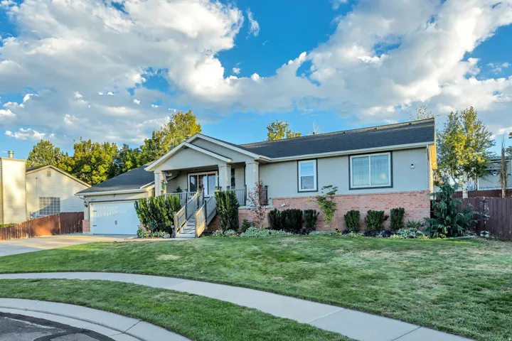 Exterior featuring a two-car garage, covered porch, brick detailing, and mature landscaping
