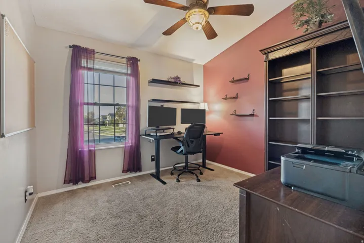 Carpeted room featuring a ceiling fan, a window with grid panes, and built-in shelving