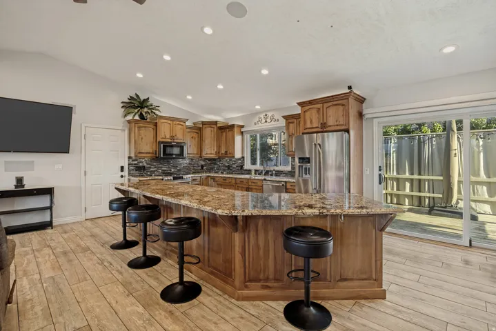 Kitchen featuring wood cabinetry, stainless steel appliances, a stone countertop island, and wood-finish flooring