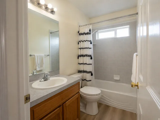 Wood-finish flooring, wood vanity with integrated sink, full-width mirror, subway tile shower surround, and transom window
