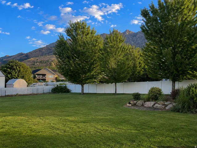 Expansive lawn area with mature trees, a white privacy fence, and a decorative rock garden