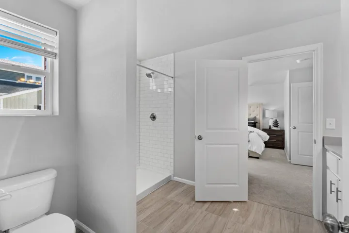 Wood-finish flooring, white subway tile shower surround, chrome shower fixture, white toilet, and white panel doors
