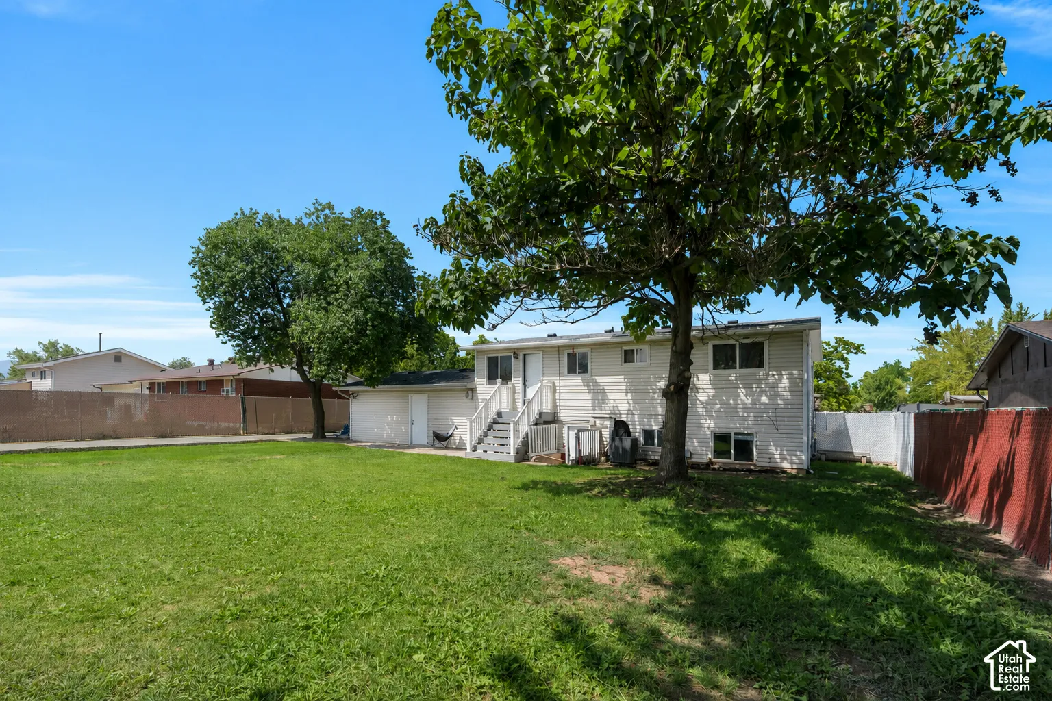 Rear view of the home showcases the expansive, private backyard, mature shade trees, and separate lower-level entrance.