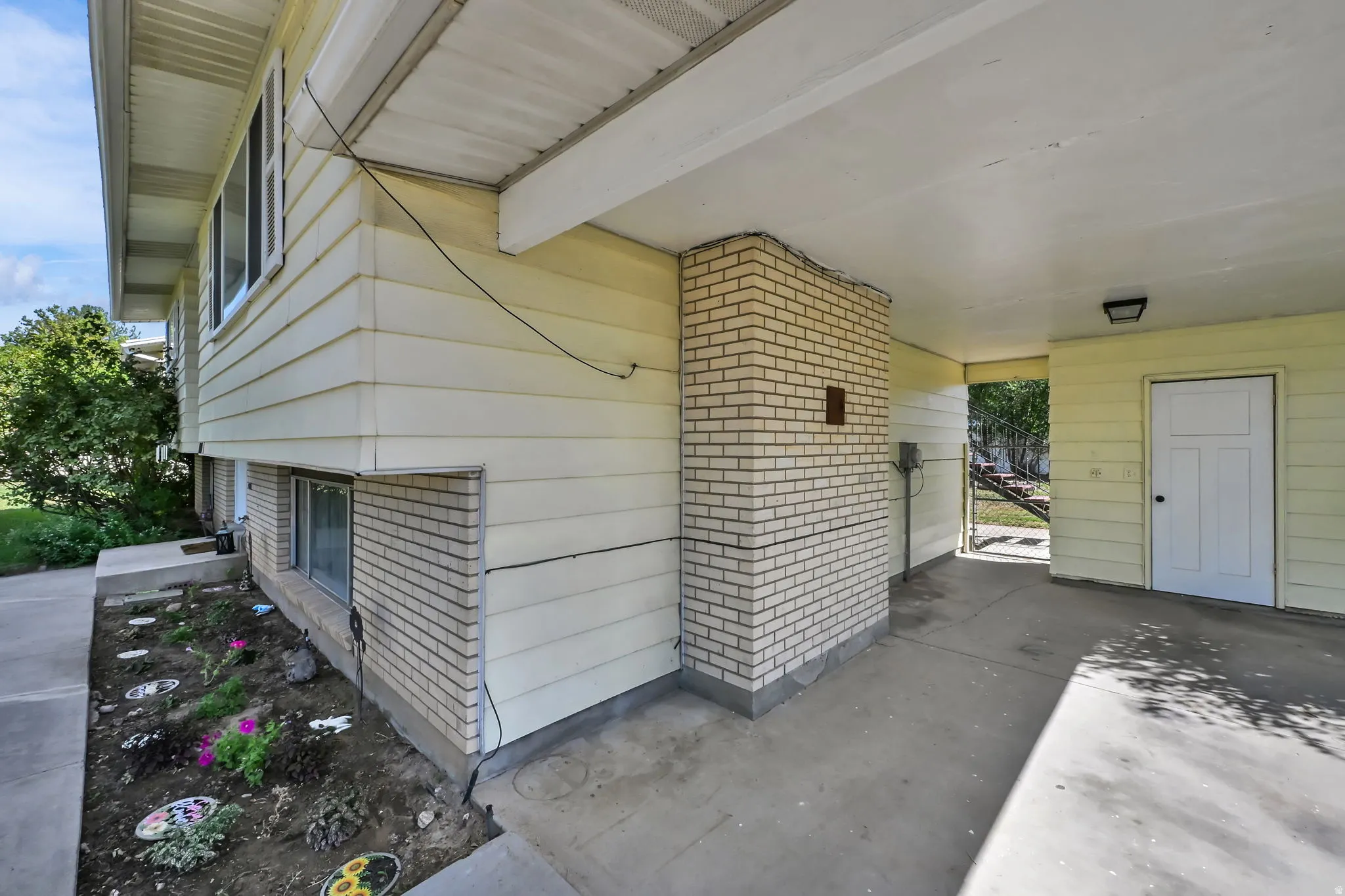 Covered carport with a concrete floor, light brick column, and a white paneled exterior door