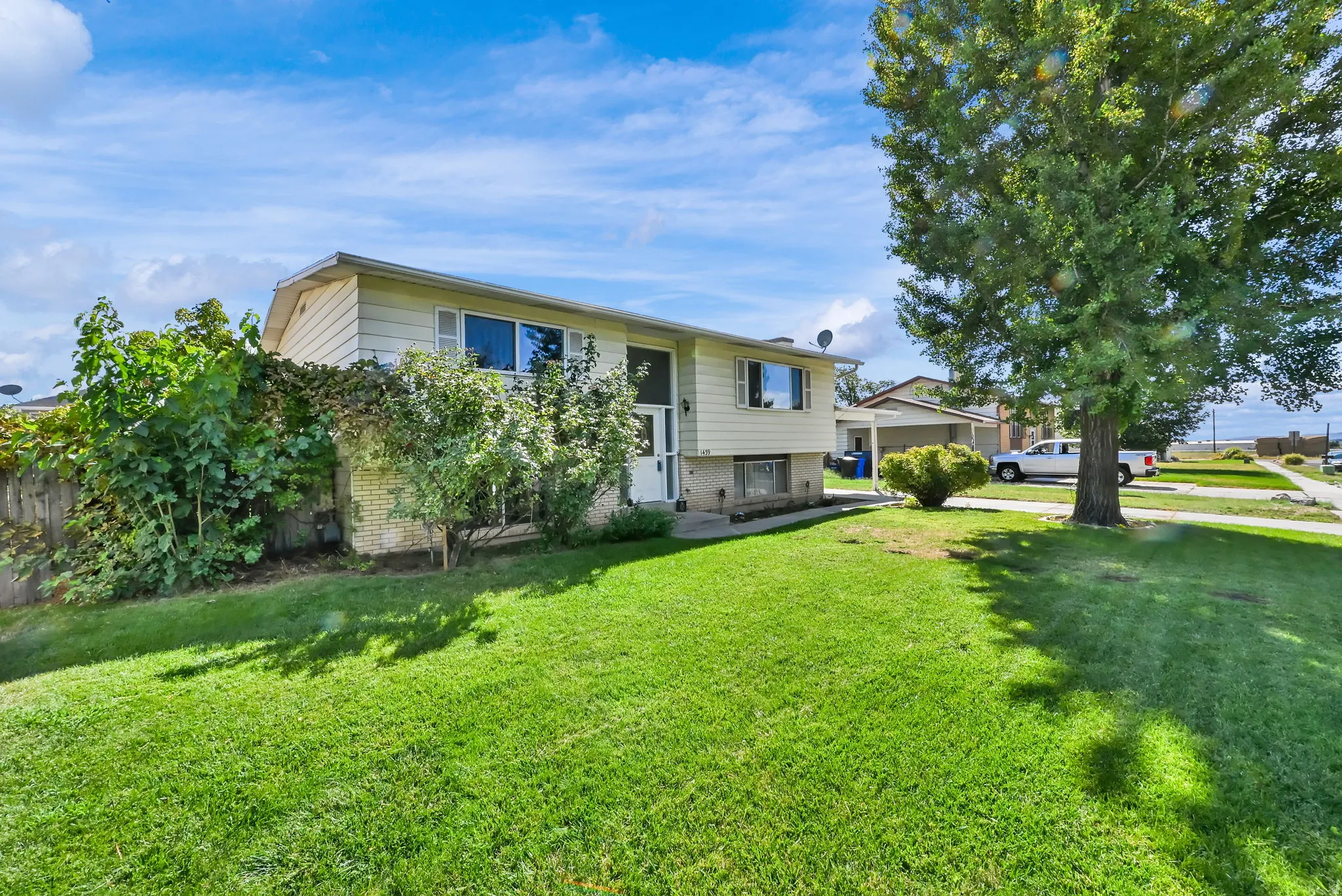 Split-level residence featuring a light-colored exterior, an expansive front lawn, and mature trees