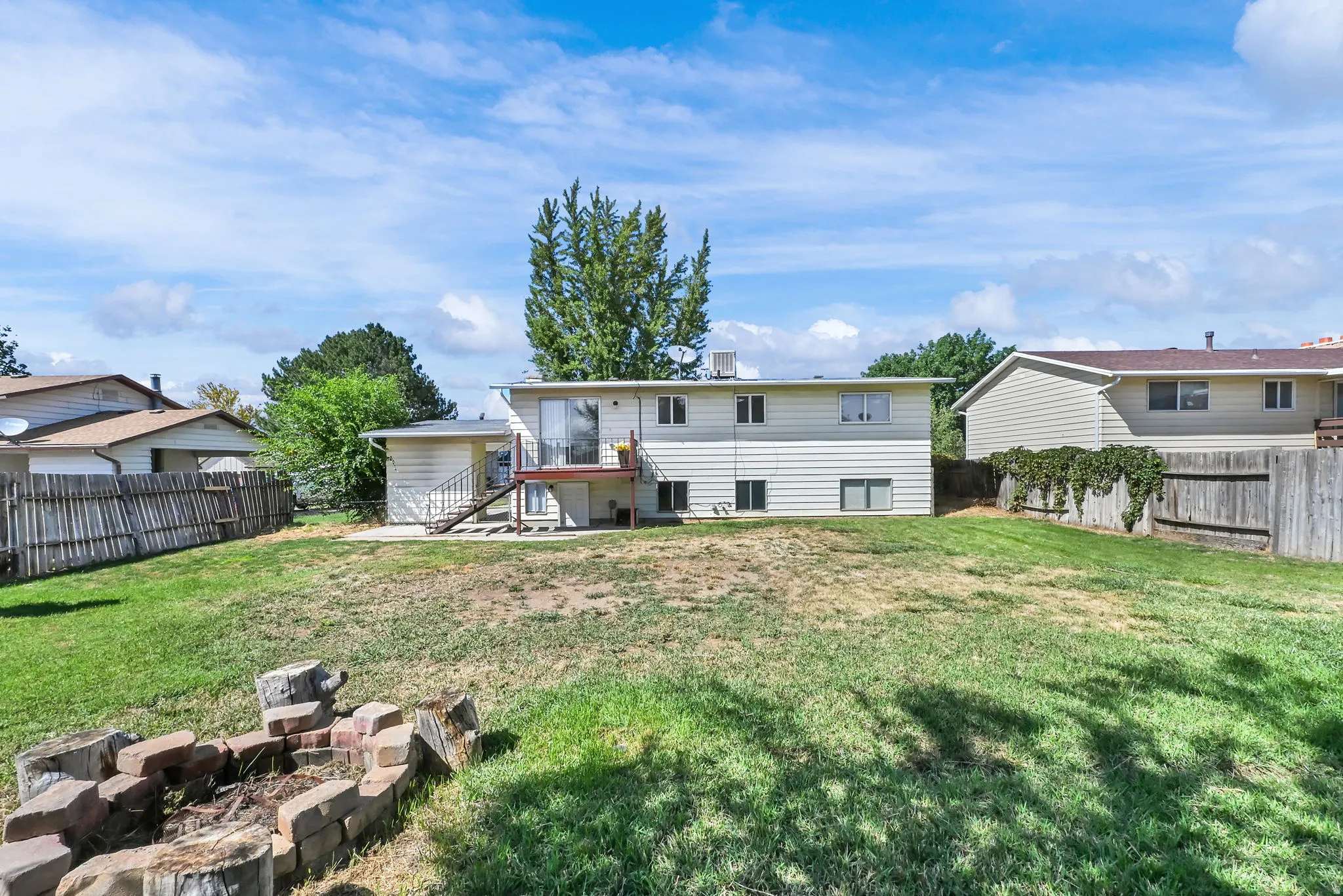 Expansive sloped yard featuring a built-in stone and wood fire pit