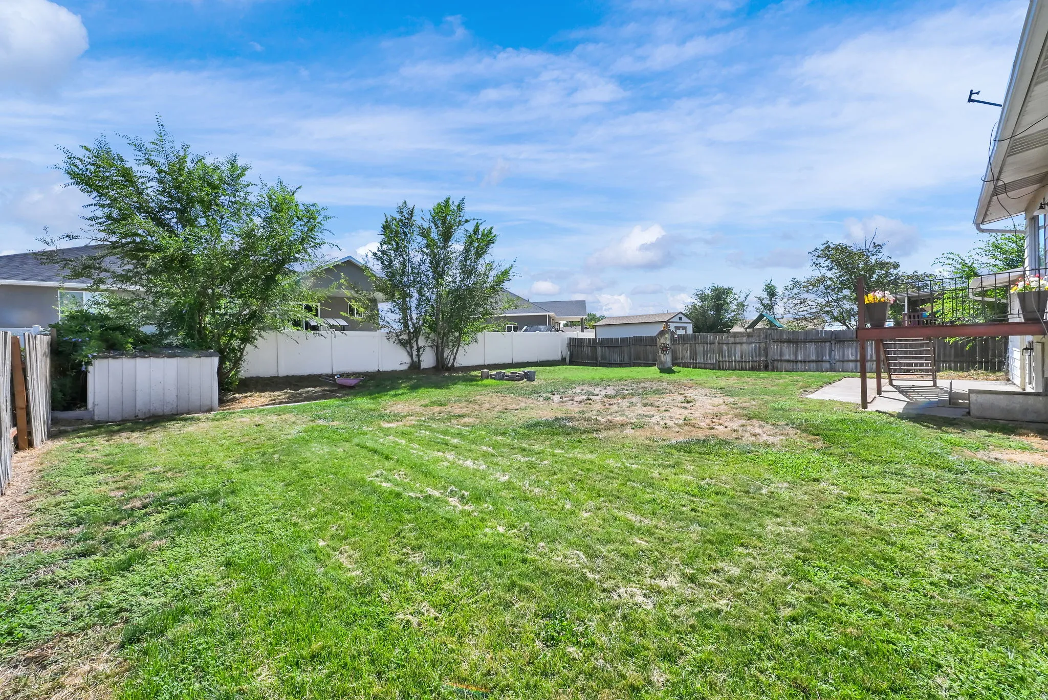 Expansive grass lawn with mature trees and a white privacy fence