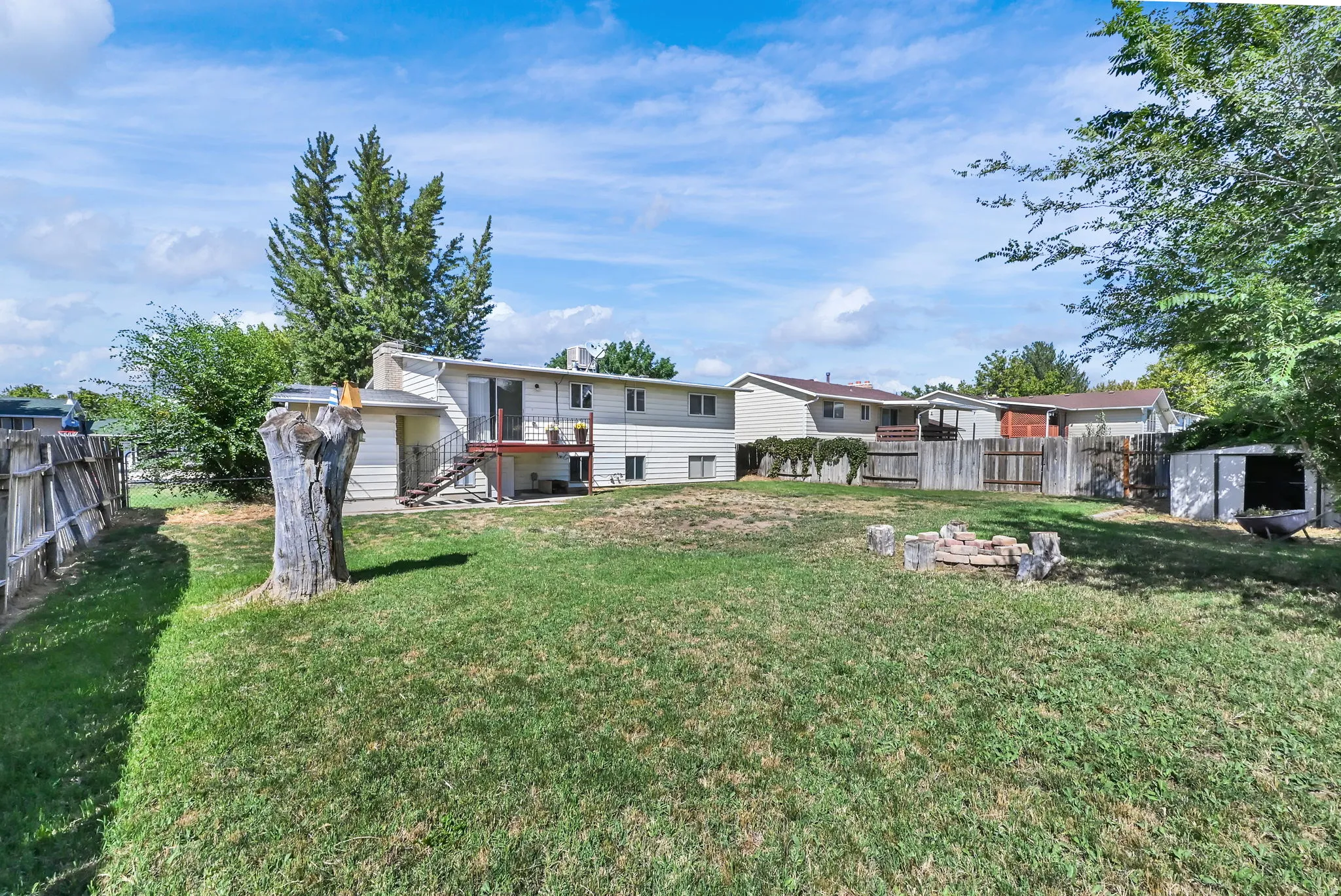 Expansive grassy yard with a wooden privacy fence, a built-in fire pit, a storage shed, and a rear exterior deck