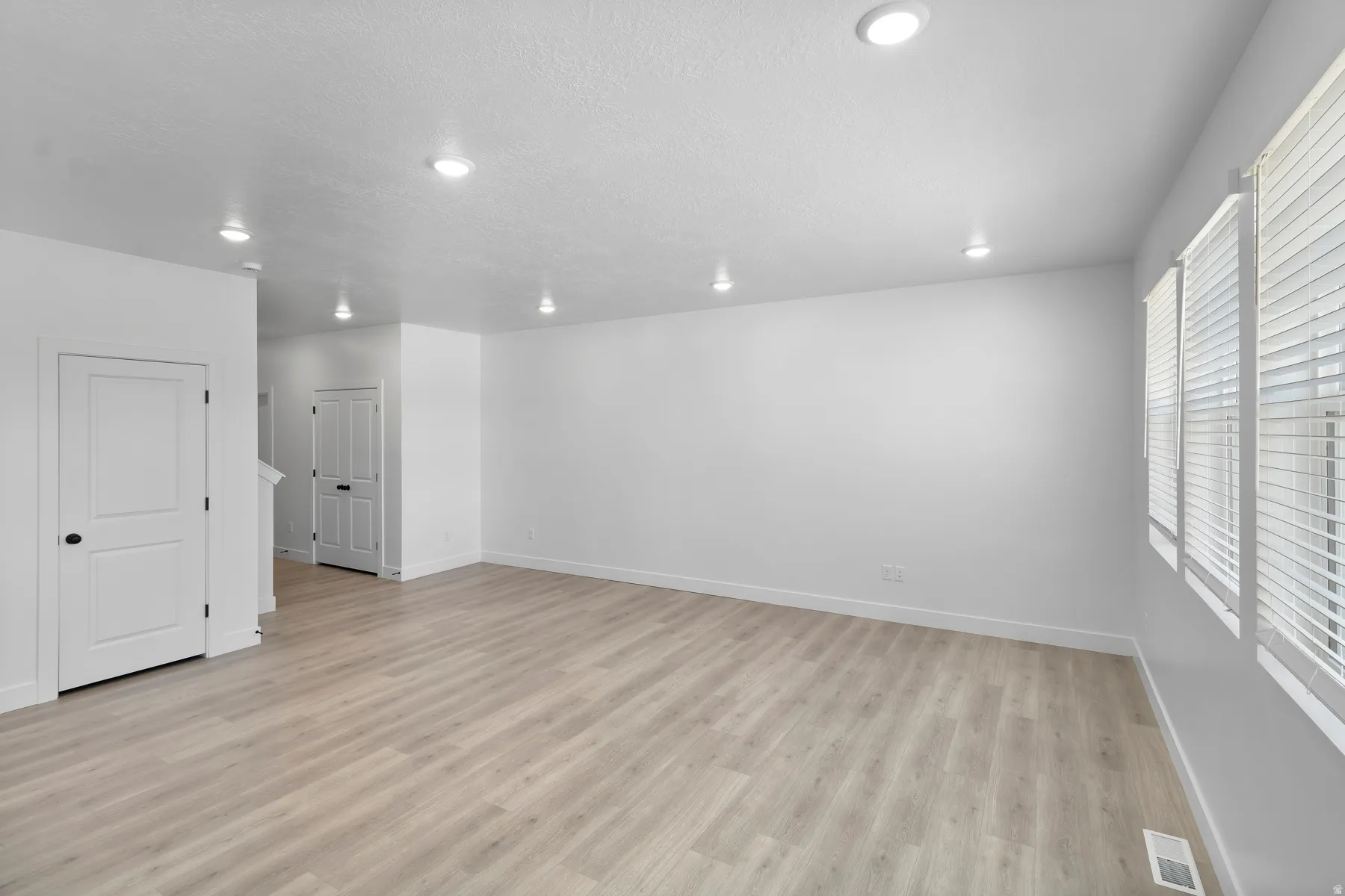 Recessed lighting, wood-finish flooring, multiple windows with horizontal blinds, and a neutral color palette