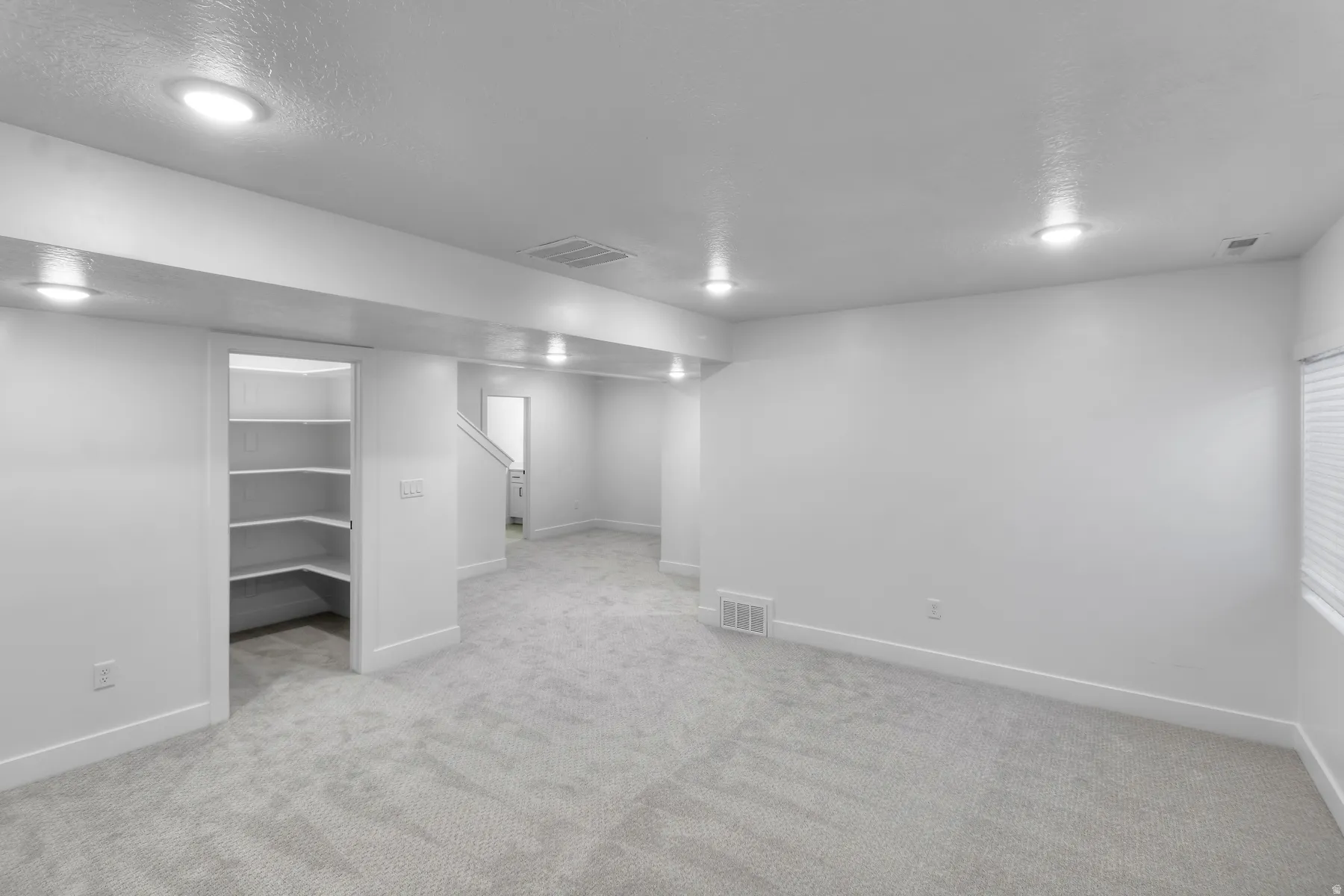 Recessed lighting, light-toned carpet, built-in shelving, white walls, and a window with blinds