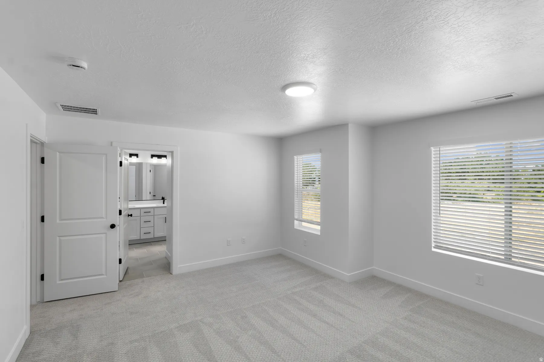 Spacious room featuring light-colored carpeting, multiple windows with blinds, and a flush-mount ceiling light