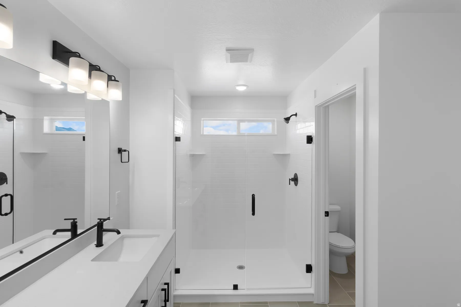 Spacious bathroom featuring a frameless glass shower enclosure, single vanity with integrated sink, black fixtures, and transom windows