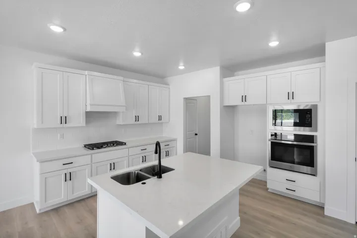 White shaker cabinetry, recessed lighting, stainless steel appliances, kitchen island with dual basin sink, and wood-finish flooring