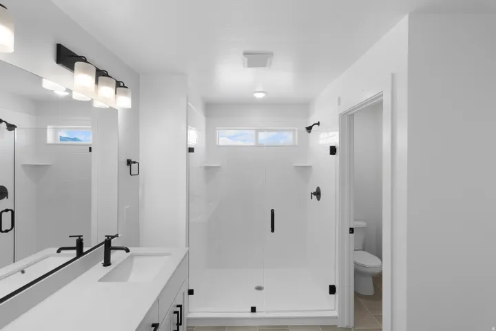 Spacious bathroom featuring a frameless glass shower enclosure, single vanity with integrated sink, black fixtures, and transom windows