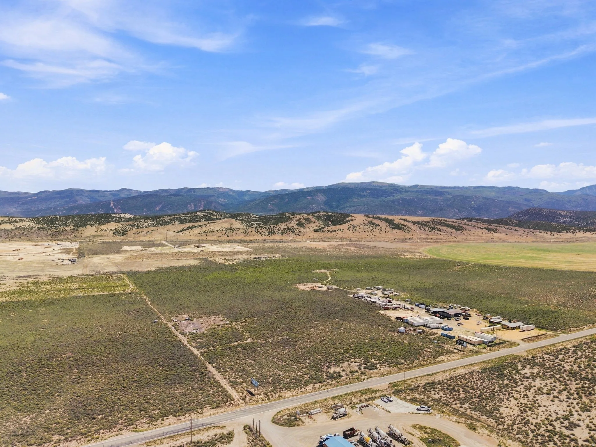 Expansive rural landscape featuring a paved road, scattered buildings, and distant mountains