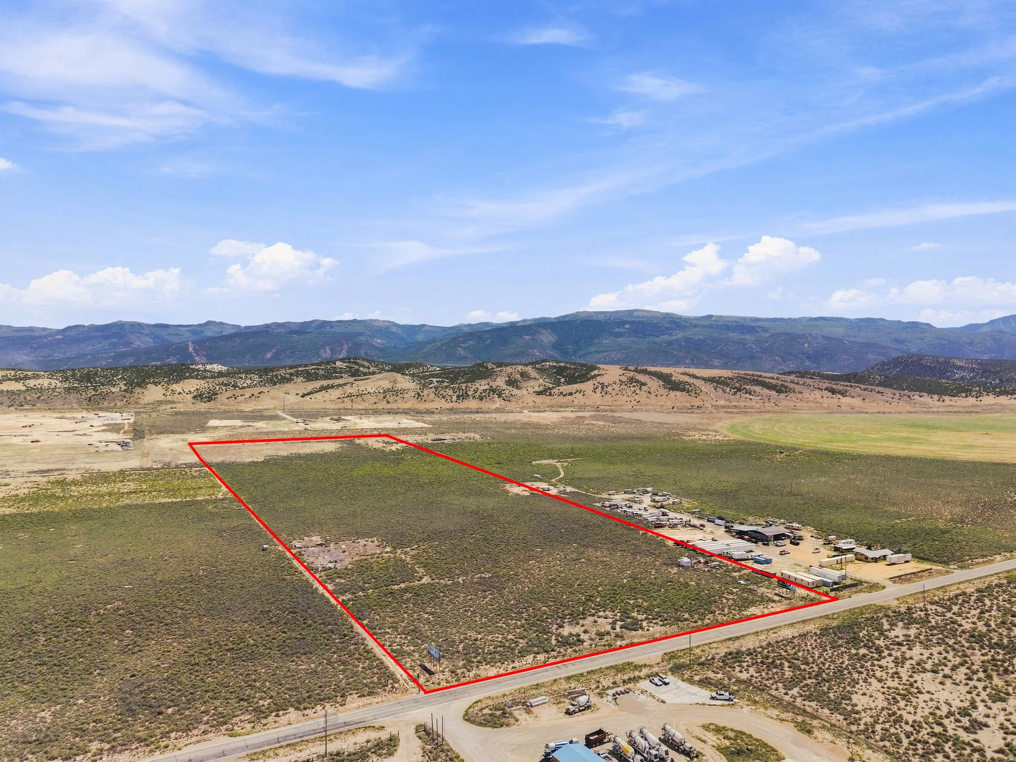 Expansive undeveloped land featuring a clear perimeter, adjacent to a paved road, with a distant mountain backdrop