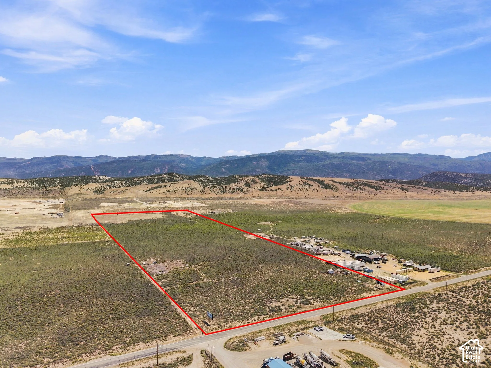 Expansive undeveloped land featuring a clear perimeter, adjacent to a paved road, with a distant mountain backdrop