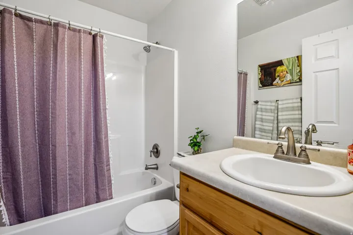 White-finished bathtub with an integrated shower, a toilet, a vanity with a laminate countertop, and a built-in mirror