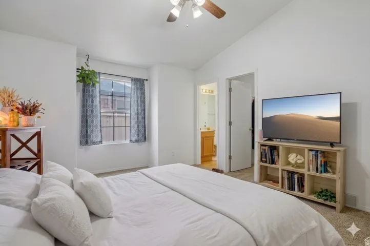 Vaulted ceiling with a ceiling fan, window with vertical blinds, and a doorway leading to a bathroom
