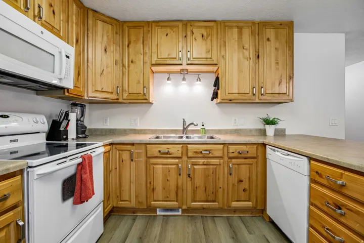 Full kitchen featuring wood cabinetry, white appliances, durable countertops, and wood-finish flooring