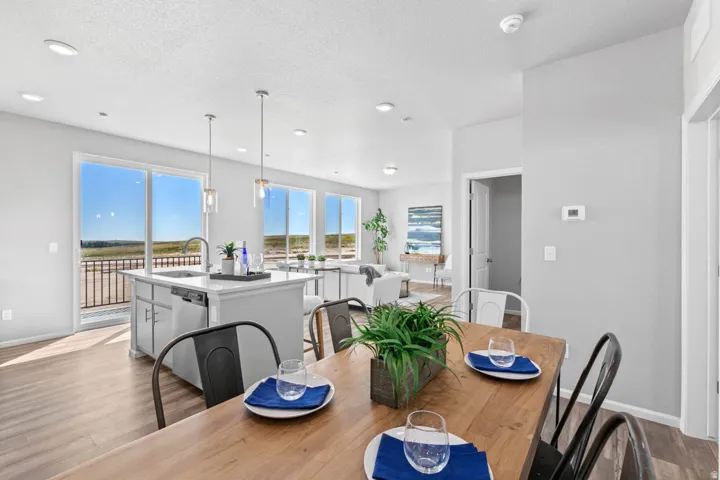 Open-concept living space with expansive windows, wood-finish flooring, a kitchen island with pendant lighting, and a sliding glass door to an outdoor balcony