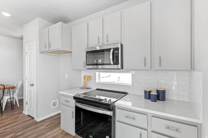 Kitchen featuring white shaker-style cabinetry, stainless steel microwave, electric range, white subway tile backsplash, and light-toned countertops
