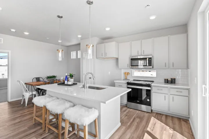Kitchen featuring a white island with an integrated sink, pendant lighting, stainless steel appliances, and wood-finish flooring