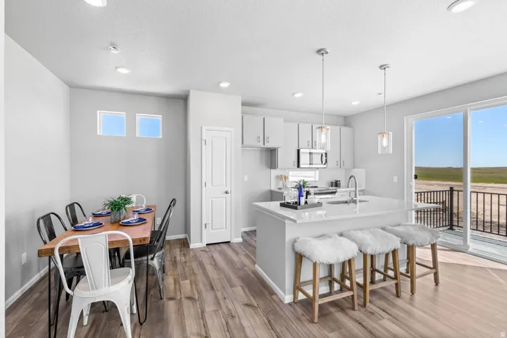 Open-concept living space with wood-finish flooring, a kitchen island, pendant lighting, and a sliding glass door leading to an outdoor deck