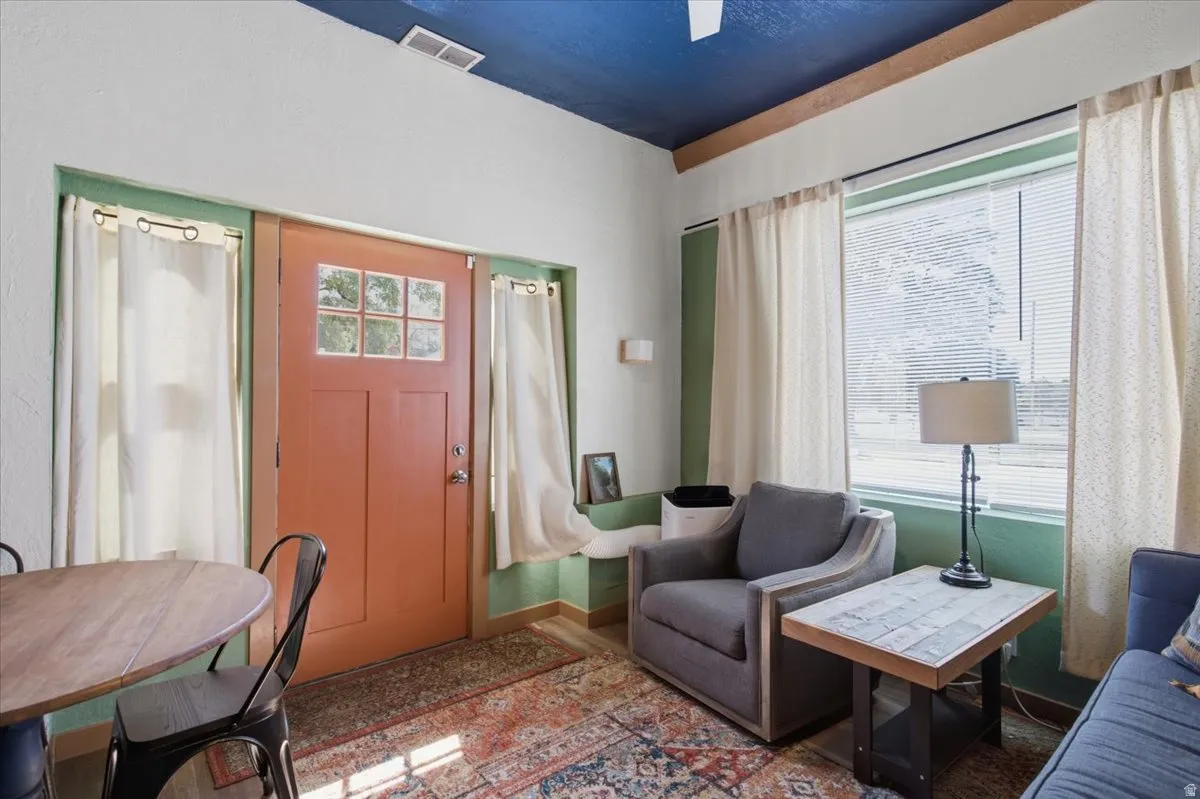 Entry door with divided lites, natural wood-finish flooring, and a window with curtains and blinds
