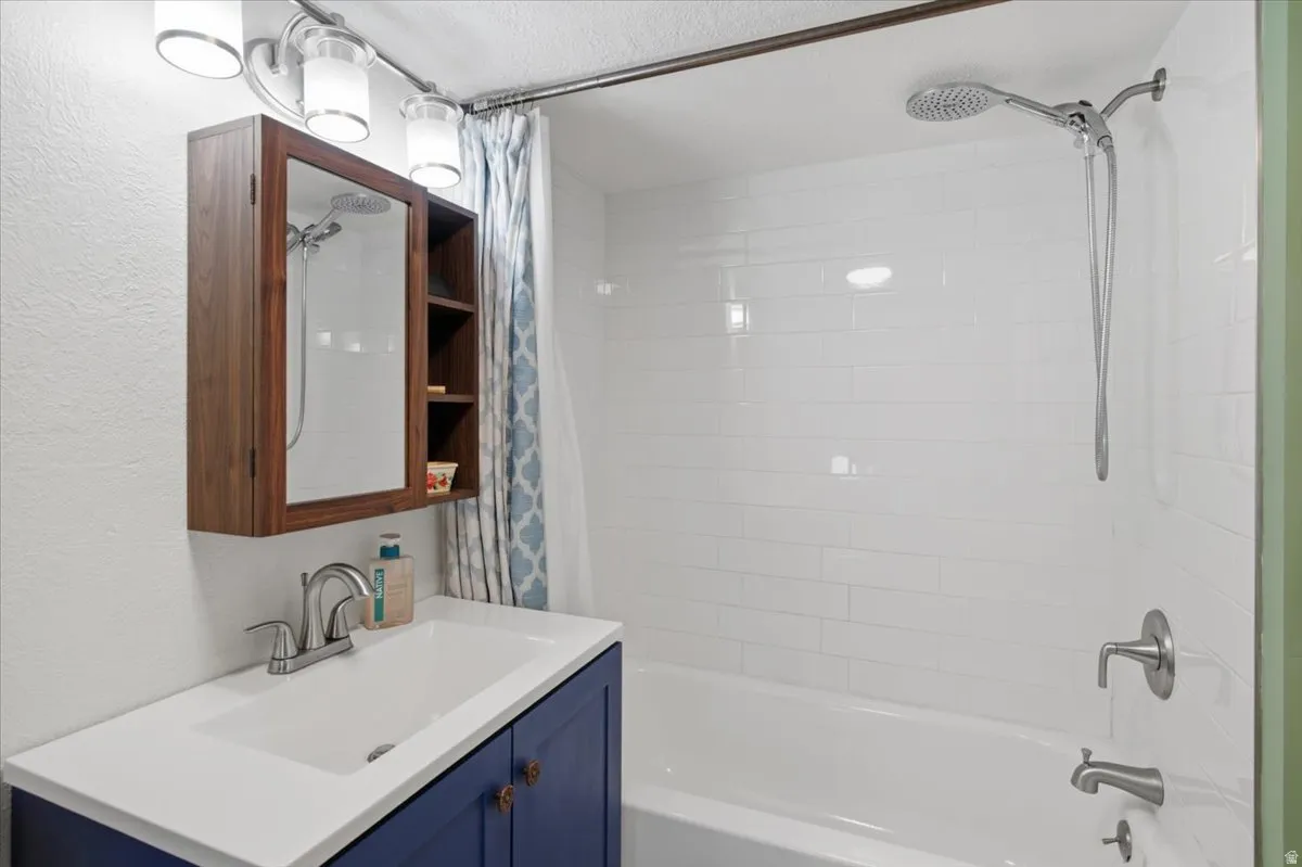Bathroom featuring a white subway tile shower surround, a white bathtub, a chrome showerhead with a handheld sprayer, a blue vanity with a white countertop, and a wood-finish medicine cabinet. Nice!