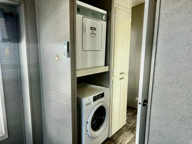 Stacked laundry appliances, built-in storage cabinetry, and wood-finish flooring