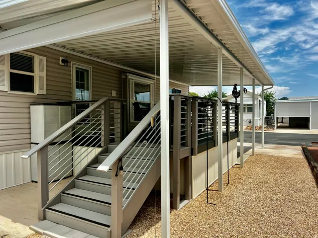 Covered outdoor structure featuring a metal roof, support columns, exterior stairs with cable railings, and a gravel ground surface