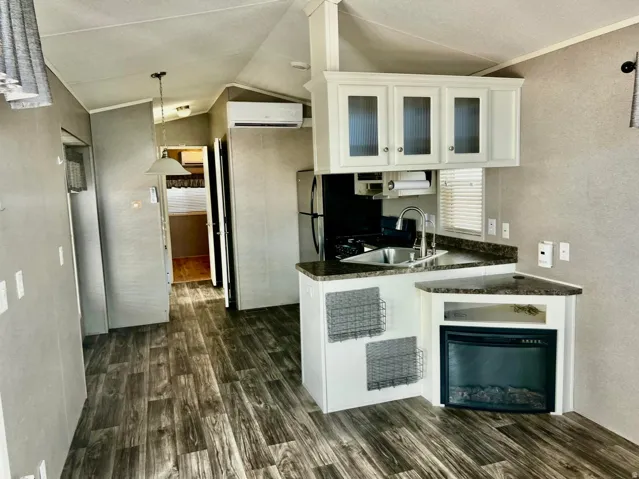 Compact kitchen featuring white cabinetry with glass-front upper doors, stainless steel sink, dark countertops, and an integrated electric fireplace