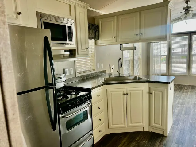 Kitchen featuring stainless steel appliances, white cabinetry, dark countertops, and wood-finish flooring