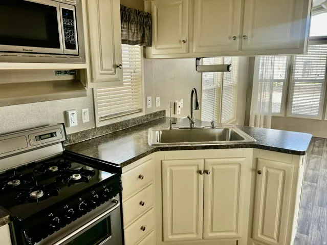 Kitchen featuring white cabinetry, dark countertops, built-in microwave, and a stainless steel sink with a high-arch faucet