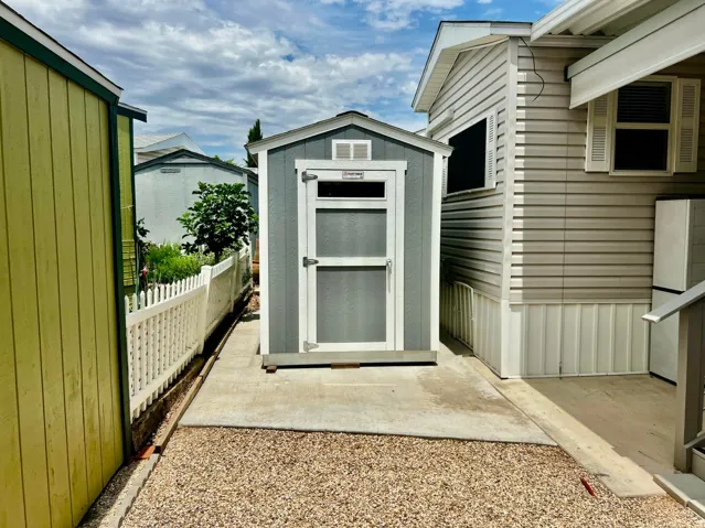 Detached storage shed with a gabled roof, light gray siding, and a white framed door