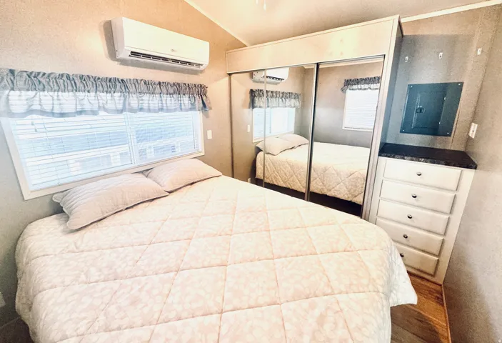 Built-in storage with a dark countertop, mirrored sliding closet doors, wall-mounted air conditioning unit, and horizontal window blinds