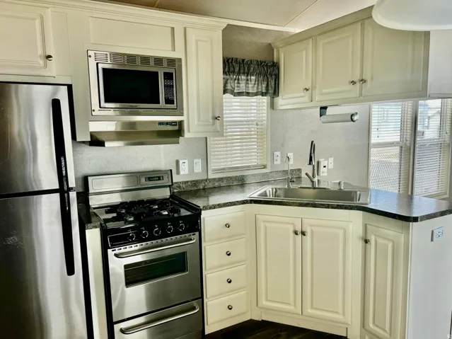 Cream-colored cabinetry with brushed nickel hardware, stainless steel appliances, dark countertops, built-in microwave, and a double-basin sink