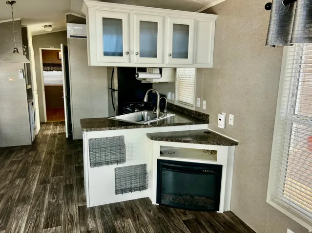 Kitchenette featuring white cabinetry with glass inserts, stainless steel sink with a gooseneck faucet, dark speckled countertops, and a built-in electric fireplace